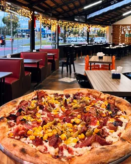 Pizza da Moriá servida no salão, com luzes e mesas ao fundo